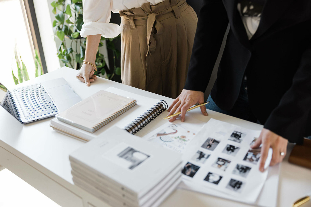 Arbeitstisch mit Notizbuch, Laptop und Fotoabzügen bei einer Design-Besprechung