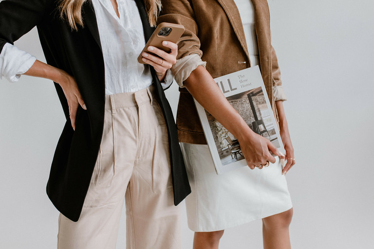 Zwei Frauen in Blazern, eine mit Smartphone, die andere mit Magazin