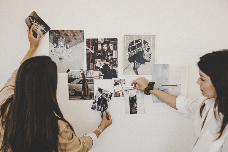 Zwei Frauen hängen Fotos für ein Moodboard an die Wand