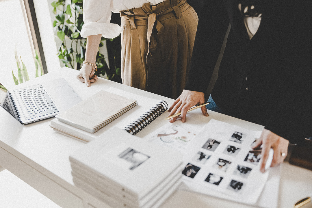 Arbeitstisch mit Notizbuch, Laptop und Fotoabzügen bei einer Design-Besprechung