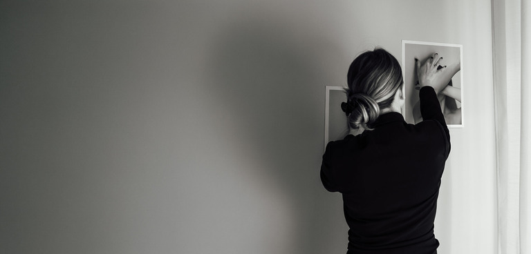 Frau richtet einen Bilderrahmen an einer grauen Wand aus