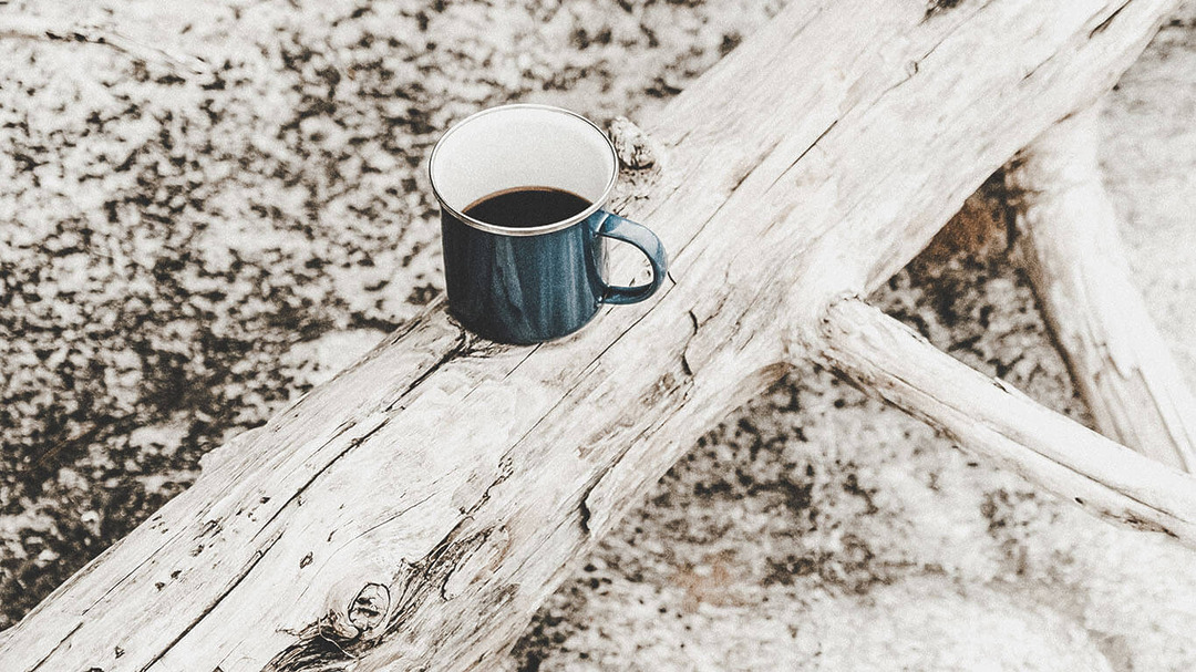Blaue Emaille-Tasse mit Kaffee auf hellem Treibholz