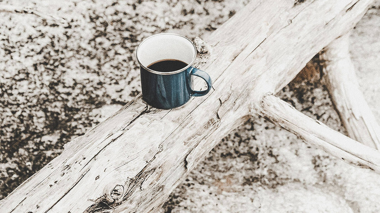 Blaue Emaille-Tasse mit Kaffee auf hellem Treibholz