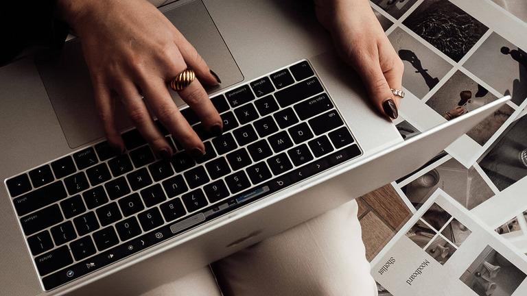 Hände auf der Laptop-Tastatur, daneben ausgelegte Schwarz-Weiß-Fotos