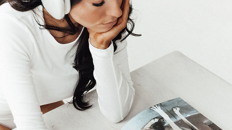 Frau in weißem Pullover stützt nachdenklich den Kopf über einem Magazin