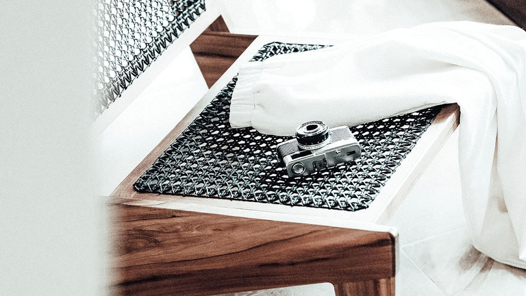Kleine Kompaktkamera auf einem Holzhocker neben weißem Stoff